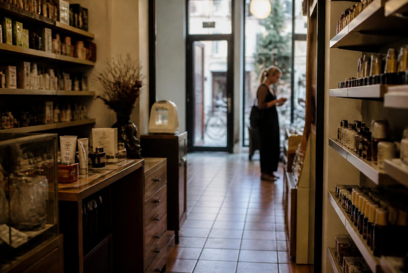 Interior de una pequeña perfumería de barrio con una clienta mirando producto al fondo