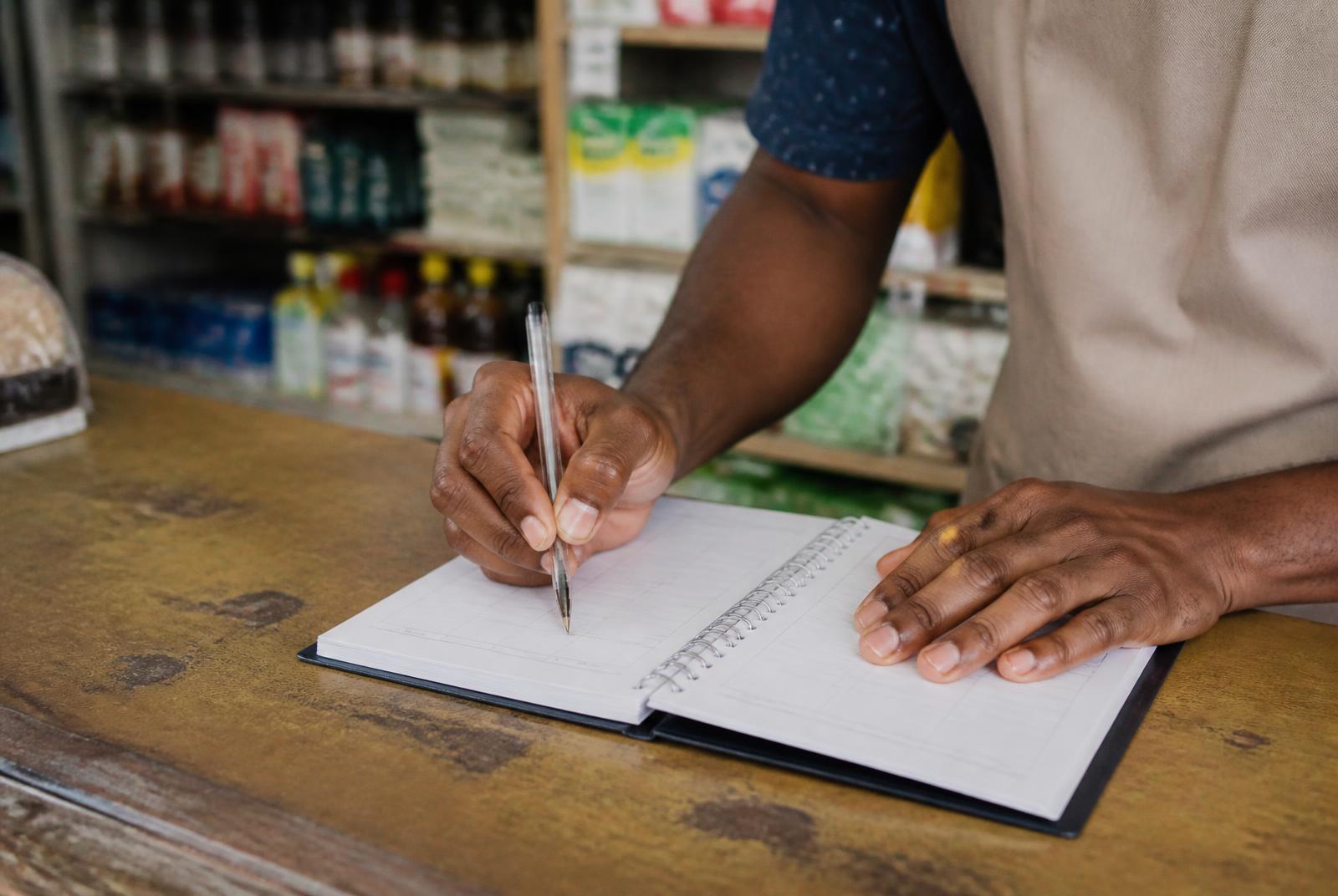 Manos escribiendo un plan de acción semanal en un cuaderno sobre el mostrador de una tienda